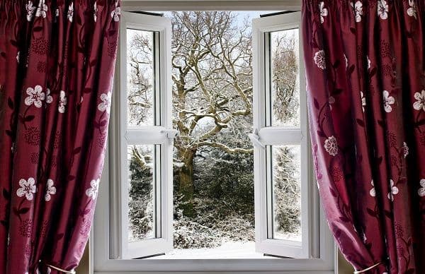 Open window framed by red curtains, revealing a snowy winter landscape with bare trees.