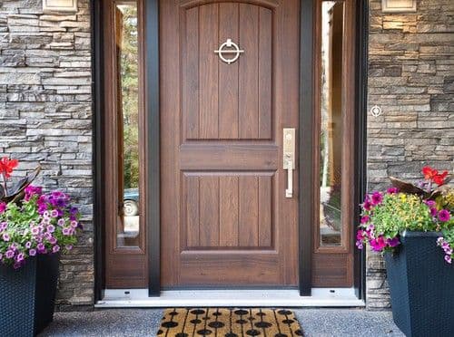 Classic wooden front door with a brass knocker, stone walls, and colorful potted flowers.