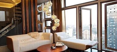 Luxurious living room with a white sofa, chaise lounge, coffee table, and city views.