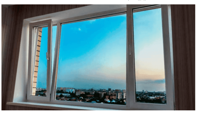 A white-framed window shows an open pane and a city skyline under a twilight sky.