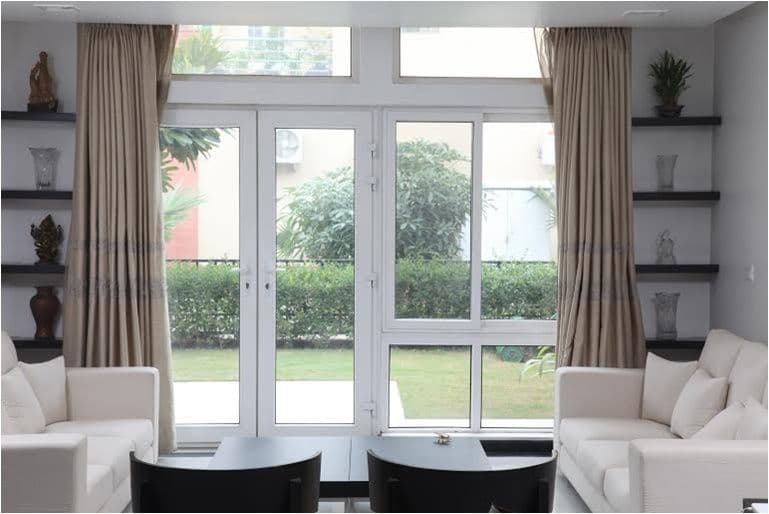 Bright living room with white sofas, glass doors opening to a green garden.