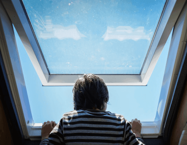 Person looking up through a large skylight at a clear blue sky.