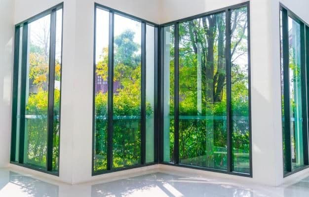 Modern room corner with large windows showcasing vibrant green trees and foliage outside.