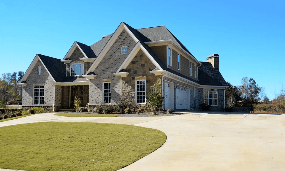 Large, modern house with stone and siding, green lawn, and wide paved driveway.