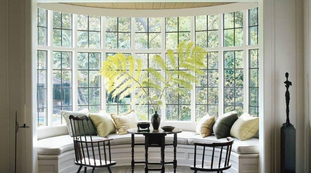 Bright bay window with built-in seat, cushions, small table, and two chairs.