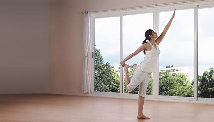 Woman in white activewear practices yoga's Dancer's Pose in a bright room.