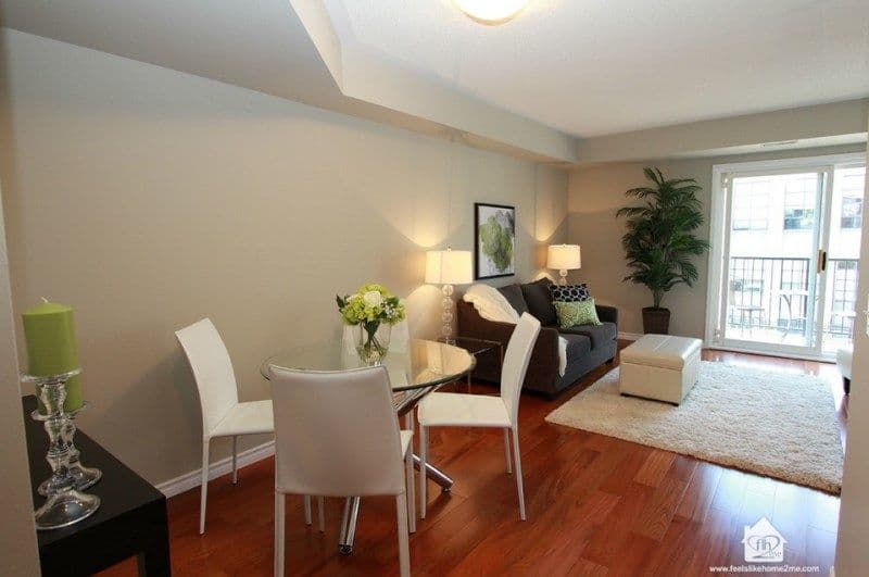 Modern open-concept living and dining room with glass table, sofa, and balcony access.