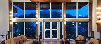 Spacious lobby with tall windows overlooking mountains and trees at dusk, with comfortable sofas.