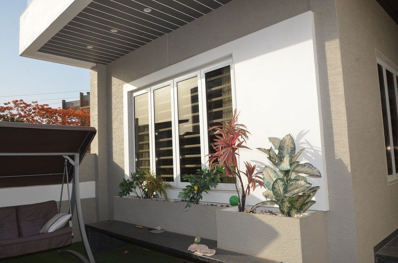 Modern house exterior with large windows, white walls, green and red foliage in planters.