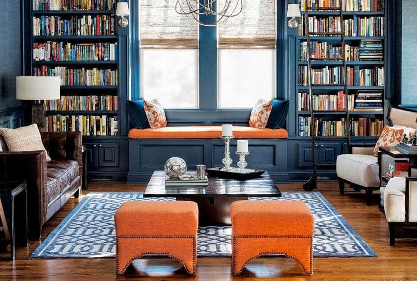 Stylish blue library features built-in bookshelves, an orange window seat, and comfortable furnishings.