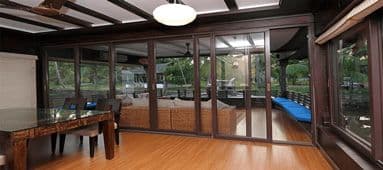Spacious indoor dining area with large glass doors opening to an outdoor patio with green foliage.