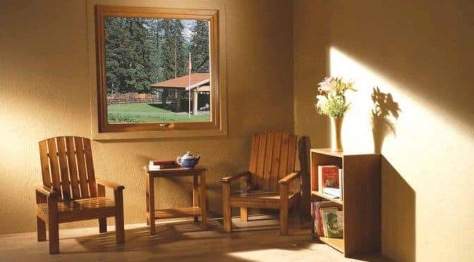 Cozy sunlit room with wooden furniture and a window view of a rustic house.