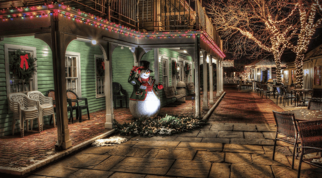 Snowman and buildings decorated with colorful Christmas lights along a festive nighttime street.