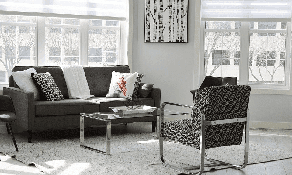 Modern living room with a gray sofa, two chairs, a coffee table, and large windows.