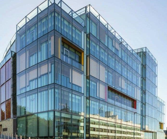 Modern glass-fronted building with reflective windows and multiple stories under a clear sky.