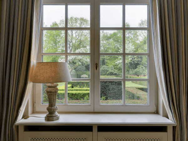 Multi-paned window with a lamp on the sill, showing a lush green garden outside.
