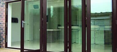 Partially open dark bi-fold glass doors reveal a bright room and reflect an outdoor view.